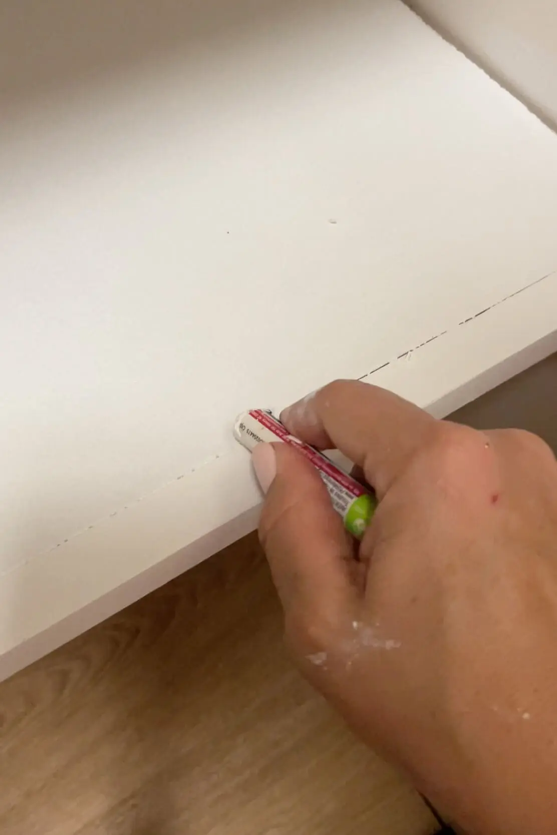 Close-up of a hand using fil-stik to smooth gaps on a newly painted white surface.